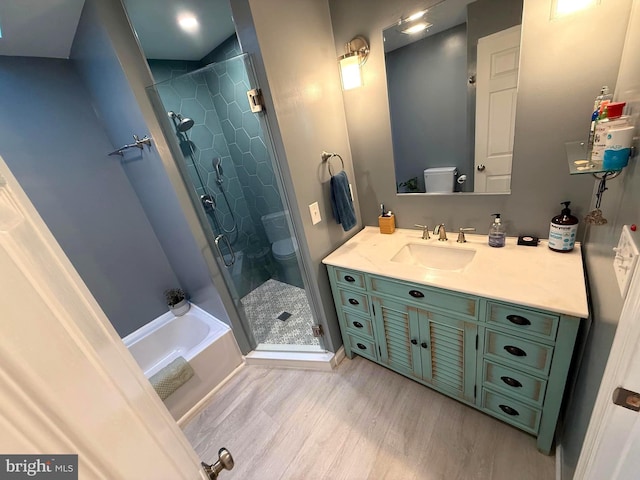 bathroom with vanity, wood finished floors, a stall shower, toilet, and a bathtub