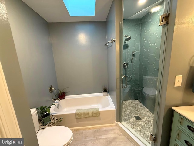 full bathroom featuring vanity, a skylight, a shower stall, a garden tub, and toilet