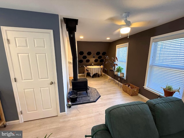 living room featuring light wood finished floors, baseboards, a wood stove, and ceiling fan