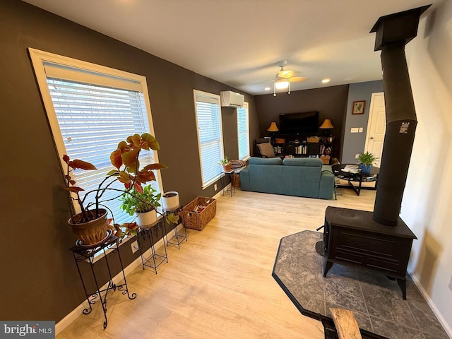 living area featuring light wood finished floors, baseboards, an AC wall unit, a wood stove, and a ceiling fan