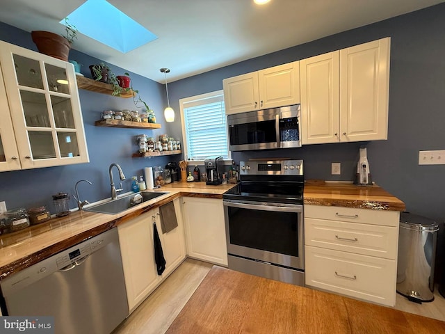 kitchen with light wood-type flooring, a skylight, white cabinets, stainless steel appliances, and a sink