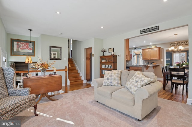 living area featuring baseboards, light wood-style flooring, recessed lighting, stairs, and a notable chandelier