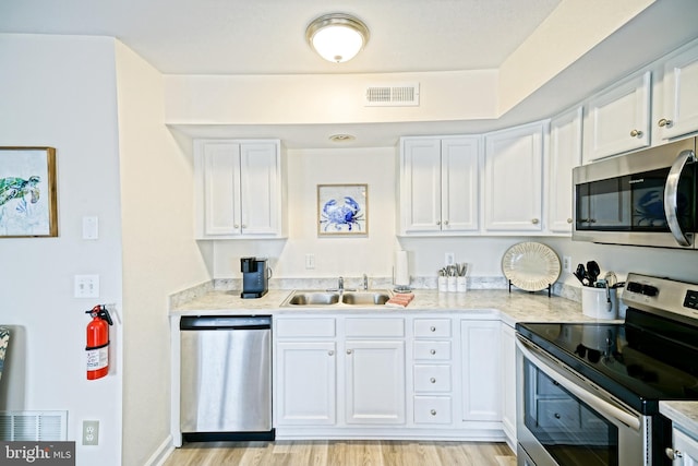 kitchen with visible vents, light wood-style flooring, appliances with stainless steel finishes, white cabinets, and a sink