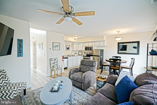 living room with a ceiling fan, light wood-style floors, and baseboards