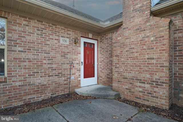 entrance to property with brick siding and a shingled roof