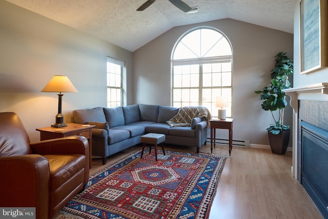 living area featuring light wood finished floors, vaulted ceiling, a tile fireplace, a ceiling fan, and a baseboard radiator