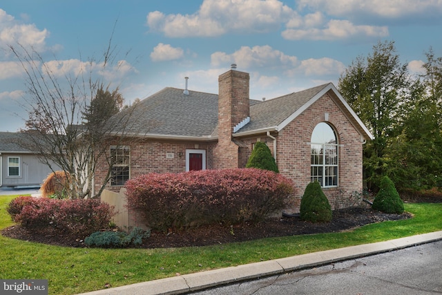 ranch-style house with a front lawn, a chimney, brick siding, and a shingled roof