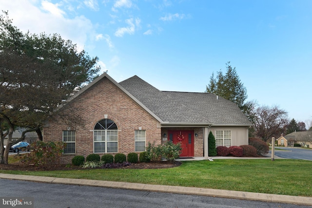 view of front of property with brick siding, a front yard, and a shingled roof