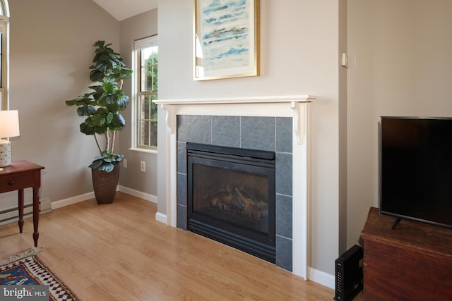 living area featuring wood finished floors, baseboards, lofted ceiling, a tile fireplace, and baseboard heating