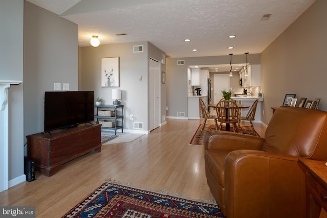 living area featuring light wood-type flooring, a textured ceiling, and visible vents