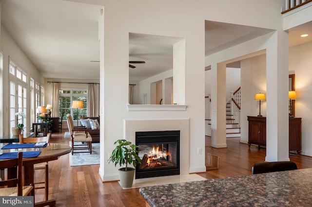 living room featuring baseboards, ceiling fan, a fireplace with flush hearth, stairway, and wood finished floors