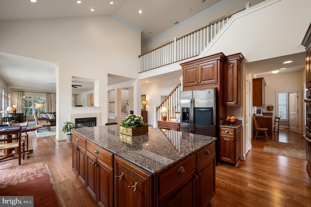 kitchen with ornamental molding, a glass covered fireplace, stainless steel appliances, dark stone counters, and dark wood-style flooring