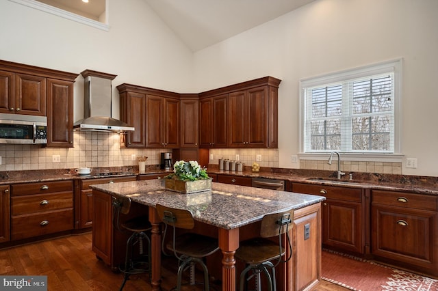 kitchen with a sink, tasteful backsplash, a center island, appliances with stainless steel finishes, and wall chimney range hood