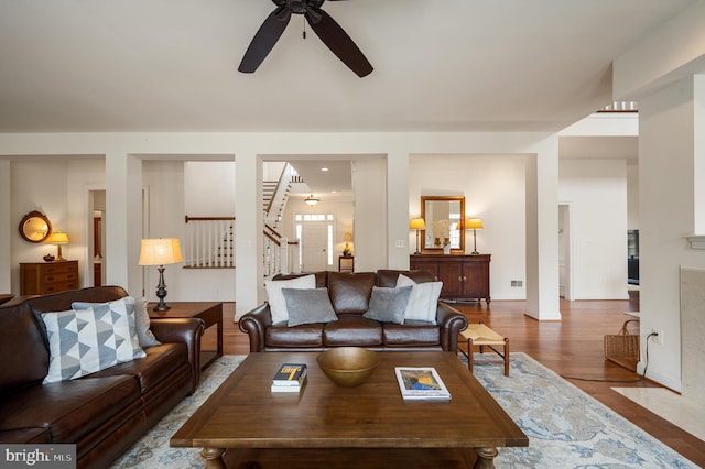 living area with stairs, wood finished floors, baseboards, and ceiling fan