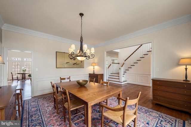 dining space featuring stairway, wood finished floors, crown molding, and a decorative wall