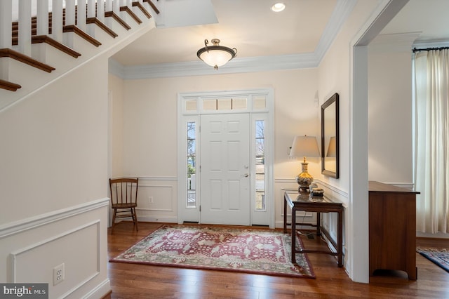 entrance foyer with crown molding, a wainscoted wall, stairway, wood finished floors, and a decorative wall