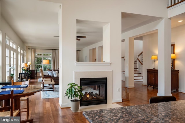 living area with a ceiling fan, wood finished floors, a multi sided fireplace, baseboards, and stairs