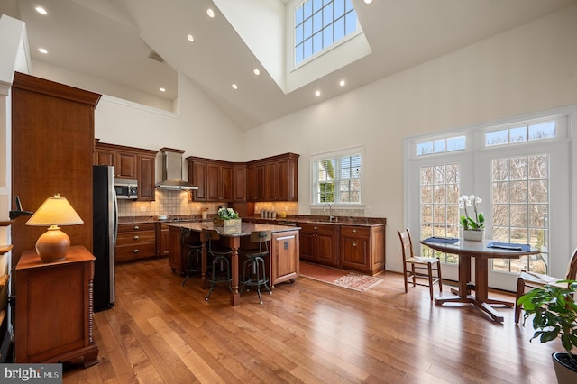 kitchen featuring a breakfast bar, light wood-style flooring, a kitchen island, stainless steel appliances, and wall chimney range hood