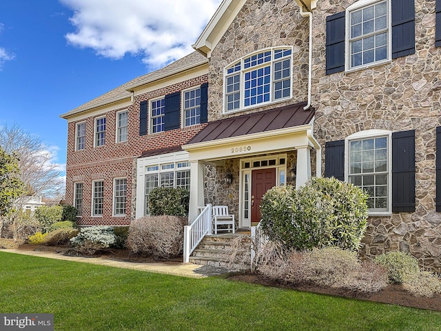 view of front facade with a standing seam roof, a front yard, stone siding, and metal roof