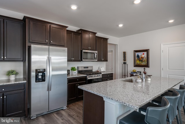 kitchen with dark wood-type flooring, a sink, a kitchen breakfast bar, stainless steel appliances, and dark brown cabinets