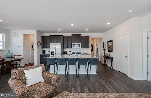 kitchen with visible vents, light countertops, an island with sink, appliances with stainless steel finishes, and dark wood-style floors