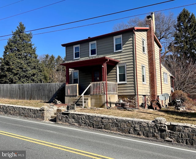 view of front of property with a porch, a chimney, and fence