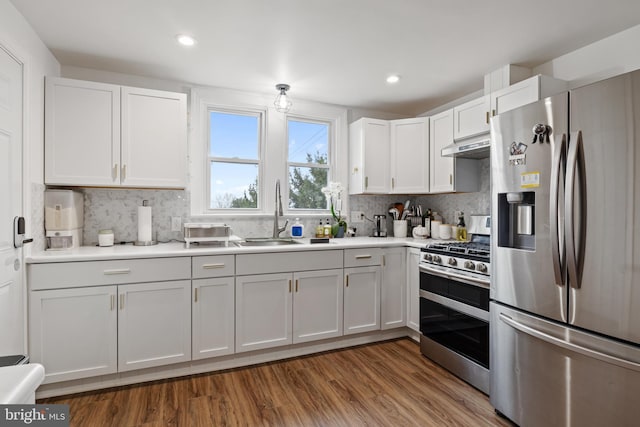 kitchen with a sink, under cabinet range hood, wood finished floors, stainless steel appliances, and white cabinets