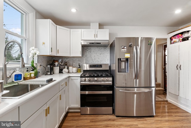 kitchen with light wood-style flooring, under cabinet range hood, a sink, appliances with stainless steel finishes, and light countertops