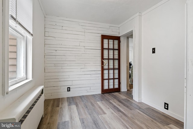 spare room featuring light wood-type flooring, a baseboard radiator, baseboards, and wooden walls