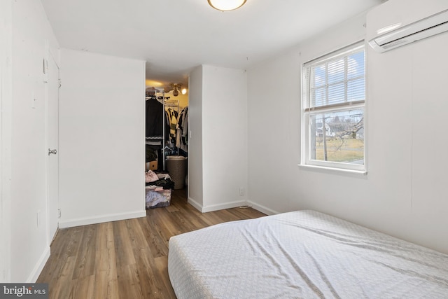 bedroom featuring wood finished floors, baseboards, a spacious closet, a closet, and a wall mounted air conditioner