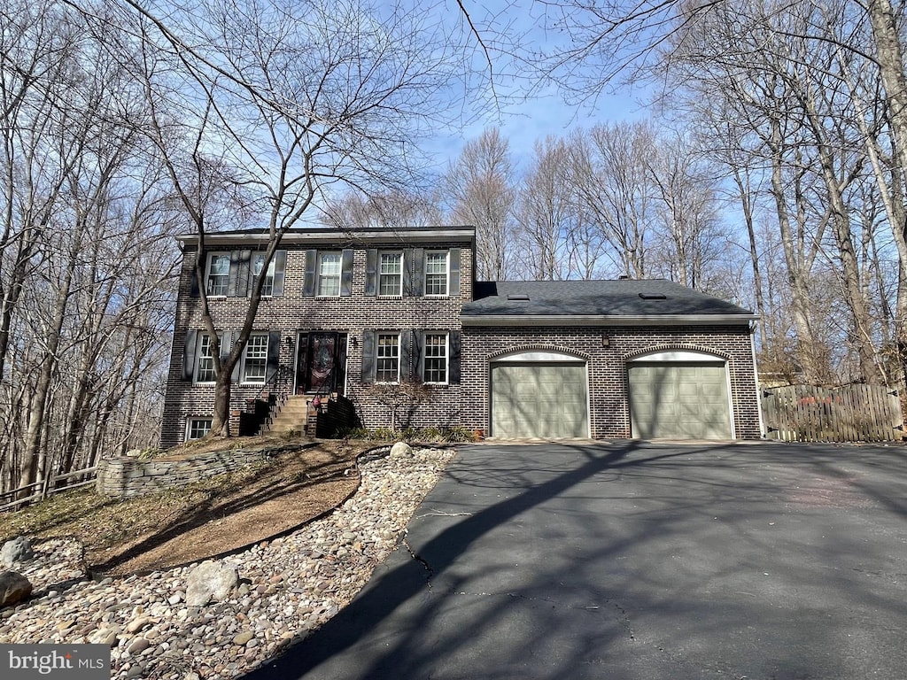 colonial-style house with brick siding, an attached garage, and driveway