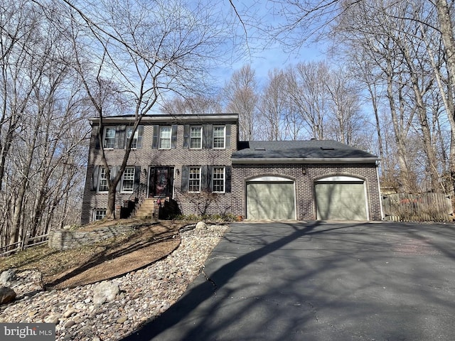 colonial-style house with brick siding, an attached garage, and driveway