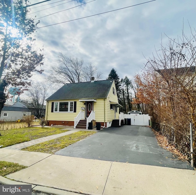 view of front facade featuring aphalt driveway, fence, roof with shingles, and entry steps