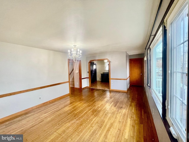 unfurnished room with light wood-type flooring, stairway, arched walkways, an inviting chandelier, and baseboards