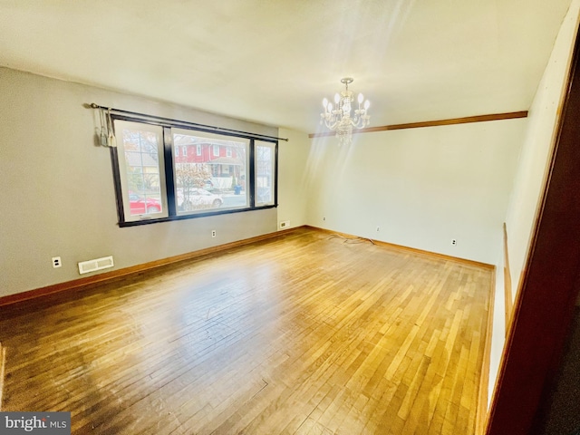 spare room featuring an inviting chandelier, baseboards, visible vents, and wood-type flooring