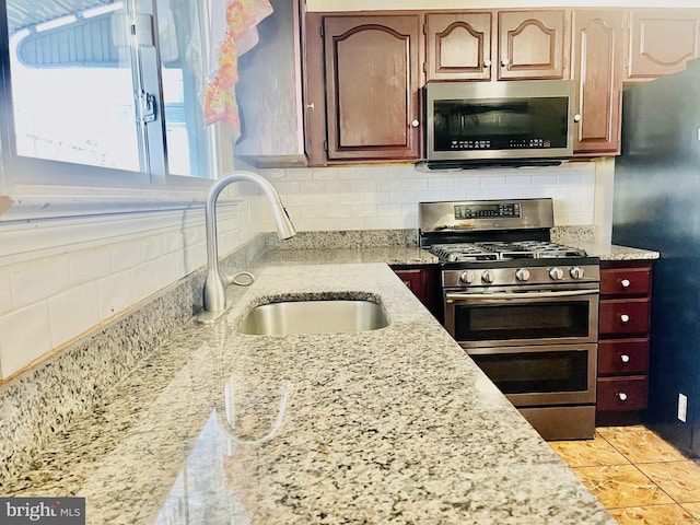 kitchen featuring a sink, decorative backsplash, light stone counters, and appliances with stainless steel finishes