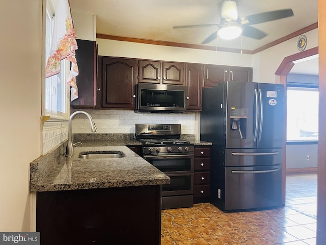 kitchen with a sink, backsplash, stainless steel appliances, dark stone counters, and dark brown cabinets