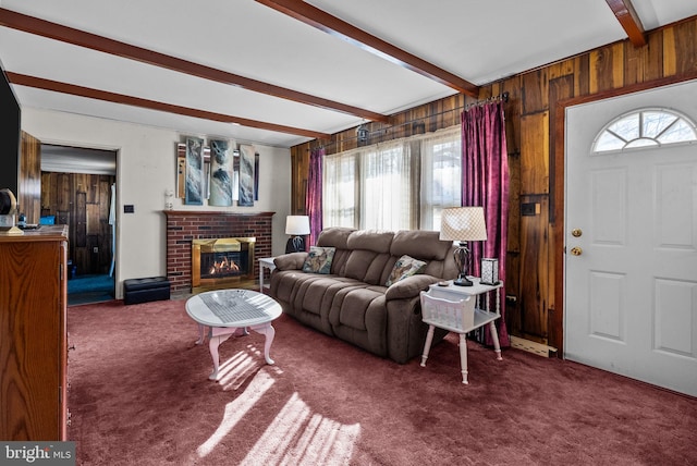 carpeted living room with beamed ceiling, a brick fireplace, and wooden walls