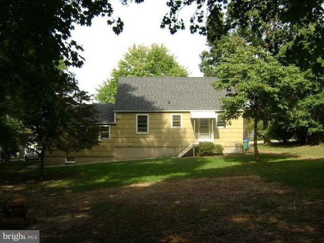 rear view of house featuring a lawn and roof with shingles