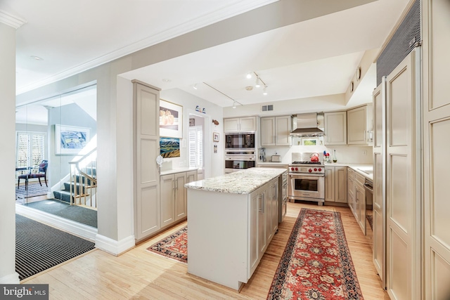 kitchen featuring visible vents, a center island, wall chimney range hood, light wood-style flooring, and appliances with stainless steel finishes