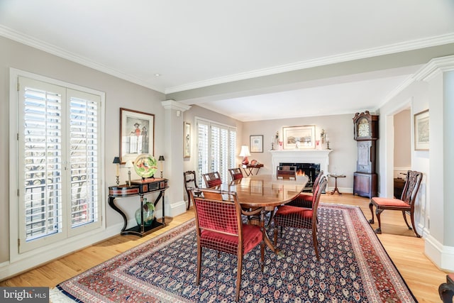 dining space with decorative columns, baseboards, a lit fireplace, and light wood-style flooring