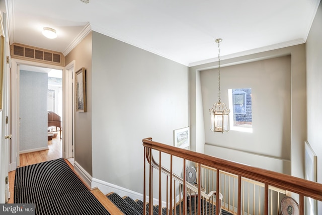 corridor with wood finished floors, visible vents, baseboards, crown molding, and an upstairs landing