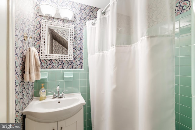 full bathroom featuring wallpapered walls, tile walls, a shower with shower curtain, wainscoting, and vanity