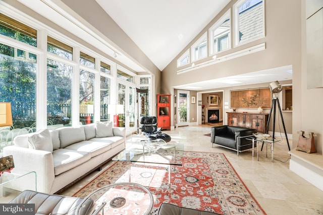 living room with high vaulted ceiling, baseboards, and a lit fireplace