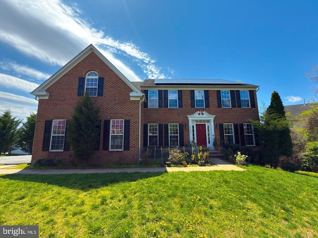 colonial inspired home featuring a front lawn, brick siding, and solar panels