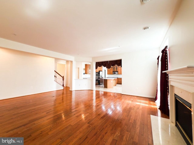 unfurnished living room featuring stairway, a high end fireplace, baseboards, and light wood-style flooring