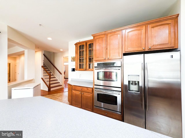 kitchen featuring brown cabinets, glass insert cabinets, light countertops, appliances with stainless steel finishes, and recessed lighting
