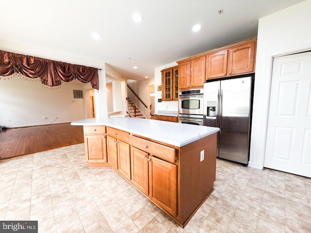 kitchen featuring stainless steel appliances, recessed lighting, glass insert cabinets, light countertops, and a kitchen island