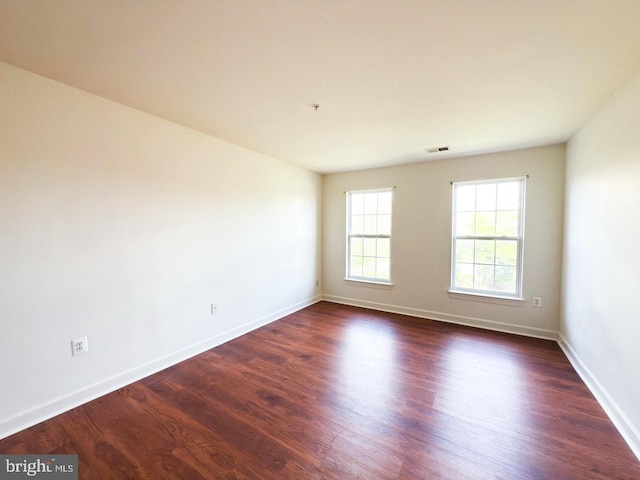 empty room featuring dark wood finished floors, visible vents, and baseboards