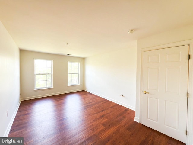 unfurnished room with baseboards and dark wood-type flooring